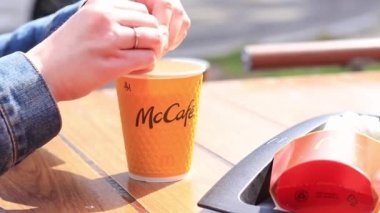 Kyiv, Ukrayna - 11 Mayıs 2023: Kadın bir McDonald 's kahvesine şeker döker. Kızın elleri bardaktaki bir içeceğe şeker döküyor. McDonald 's' da anlık kahve. McDonalds restoranında sarı McCafe kapuçino.