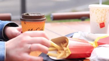Kyiv, Ukrayna - 11 Mayıs 2023: Kız McDonalds 'da açık hava masasında yemek yiyor. Kız fast food yiyor. Kadın eli patates kızartması alır. McDonald 's Corporation dünyanın en büyük fast food restoranıdır.