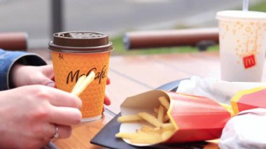 Kyiv, Ukrayna - 11 Mayıs 2023: Kız McDonalds 'da açık hava masasında yemek yiyor. Kız fast food yiyor. Kadın eli patates kızartması alır. McDonald 's Corporation dünyanın en büyük fast food restoranıdır.