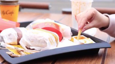 Kyiv, Ukrayna - 11 Mayıs 2023: Kız McDonalds 'da açık hava masasında yemek yiyor. Kız fast food yiyor. Kadın eli patates kızartması alır. McDonald 's Corporation dünyanın en büyük fast food restoranıdır.