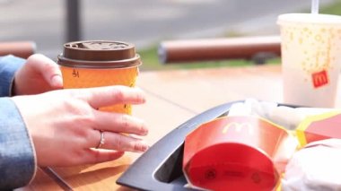 Kyiv, Ukrayna - 11 Mayıs 2023: McDonald 's' dan fast food. Kahve ve patates kızartmasıyla yakın plan kadın eli. Açık hava masasında yemek. Seçici odak