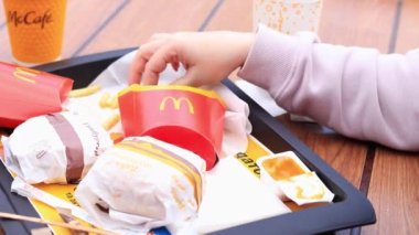 Kyiv, Ukrayna - 11 Mayıs 2023: Kız McDonalds 'da açık hava masasında yemek yiyor. Kız fast food yiyor. Kadın eli patates kızartması alır. McDonald 's Corporation dünyanın en büyük fast food restoranıdır.