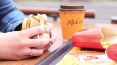 Kyiv, Ukrayna - 11 Mayıs 2023: Bir kız açık hava masasında McDonald 's çizburgeri yiyor. Fast food restoranında hamburger yiyen bir kadın. McDonald 's Şirketi