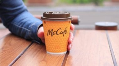 Kyiv, Ukrayna - 11 Mayıs 2023: McDonalds restoranında sarı McCafe bardağı kapuçino. Dışarıda latte içeriz. Bir kadının eli, yakın plan kahveli bir kağıt bardak alır.