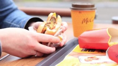 Kyiv, Ukrayna - 11 Mayıs 2023: Bir kız açık hava masasında McDonald 's çizburgeri yiyor. Fast food restoranında hamburger yiyen bir kadın. McDonald 's Şirketi