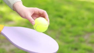 Yeşil bir top ve temiz havada tenis oynamak için parlak bir raket. İyi havalarda hobiler ve dinlenme. Kadın eli topa yakın çekimde tahta bir raketle vuruyor.