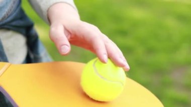 Dişi eller ahşap bir raket ve yakın plan bir top tutuyor. İyi havalarda hobiler ve dinlenme. Yeşil bir top ve parlak bir tenis raketi. Açık hava spor aktivitesi