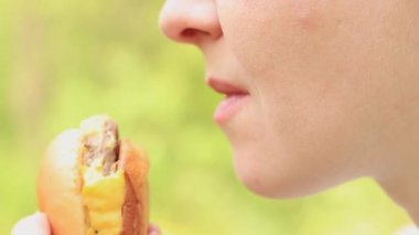 Kız fast food restoranından bir çizburger yiyor. Yakın plan bir burger ısır. Lezzetli fast food, zevkle fast food yiyin. Bir kadın iştah açıcı bir şekilde hamburger yer.