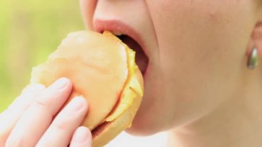 Kız fast food restoranından bir çizburger yiyor. Yakın plan bir burger ısır. Lezzetli fast food, zevkle fast food yiyin. Bir kadın iştah açıcı bir şekilde hamburger yer.