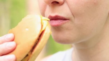 Kız fast food restoranından bir çizburger yiyor. Yakın plan bir burger ısır. Lezzetli fast food, zevkle fast food yiyin. Bir kadın iştah açıcı bir şekilde hamburger yer.
