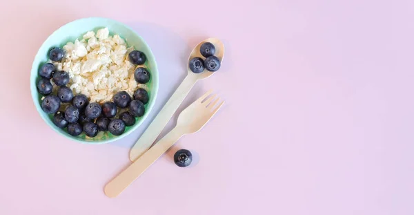 stock image Healthy breakfast. Cottage cheese with blueberries in a plate on a light pink background, top view. Healthy keto breakfast concept. Healthy breakfast plate, cloth napkin, wooden spoon and fork