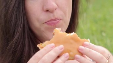 Kyiv, Ukrayna - 22 Mayıs 2023: Yakın plan bir kadının yüzü doğada bir çizburger yer. Lezzetli bir burger yiyen aç genç bir kadın. Kadının ağzı yemek çiğniyor. McDonald's