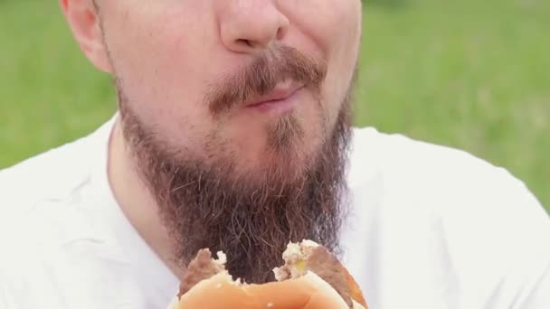 吃一个汉堡 密切的男性脸吃芝士汉堡 饥饿的留着胡子的年轻人吃着美味的汉堡包 那家伙的嘴在咀嚼食物 小菜一碟 — 图库视频影像