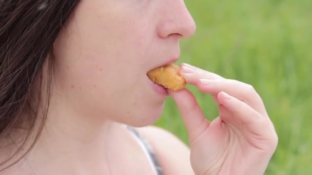 少女は鶏の切り身やナゲットを食べる 空腹の若い女性がファーストフードを食べている 自然の中で軽食 女の口が鶏のナゲットを噛んでる — ストック動画