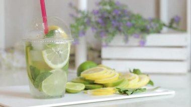 Ev yapımı mojito veya limonata. Bir kadının eli soğuk bir yaz içeceğiyle plastik bir bardak alır. Hafif bir mutfakta serinletici bir içeceği olan plastik bir bardak.