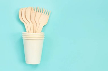 Kağıt bardakta tek kullanımlık tahta çatallar ve kaşıklar, üst manzara. Çevre dostu tek kullanımlık mutfak aletleri mavi arka planda, kopyalama alanı. Düz yatıyordu. Ekolojik yemek konsepti
