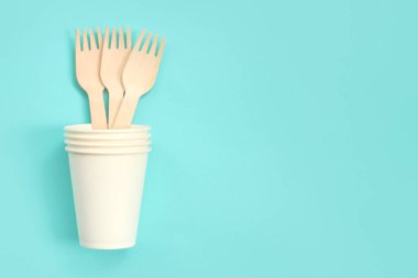 Beyaz kağıt bardakta tek kullanımlık tahta çatallar, üst manzara. Çevre dostu tek kullanımlık mutfak aletleri mavi arka planda, kopyalama alanı. Düz yatıyordu. Ekolojik yemek konsepti