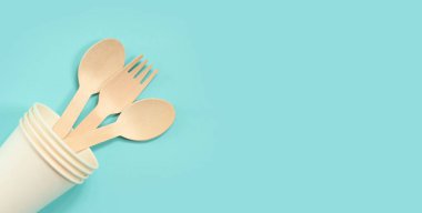 Kağıt bardakta tek kullanımlık tahta çatallar ve kaşıklar, üst manzara. Çevre dostu tek kullanımlık mutfak aletleri mavi arka planda, kopyalama alanı. Düz yatıyordu. Ekolojik yemek konsepti
