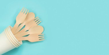 Kağıt bardakta tek kullanımlık tahta çatallar ve kaşıklar, üst manzara. Çevre dostu tek kullanımlık mutfak aletleri mavi arka planda, kopyalama alanı. Düz yatıyordu. Ekolojik yemek konsepti