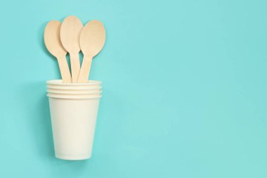 Beyaz kağıt bardakta tek kullanımlık tahta kaşıklar, üst manzara. Çevre dostu tek kullanımlık mutfak aletleri mavi arka planda, kopyalama alanı. Düz yatıyordu. Ekolojik yemek konsepti