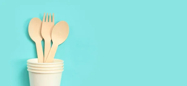 stock image Wooden disposable forks and spoons in a paper cup, top view. Eco friendly disposable kitchen utensils on a blue background, copy space. Flat lay. The concept of ecological dishes