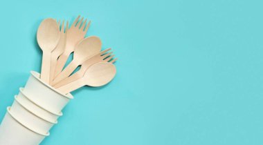 Kağıt bardakta tek kullanımlık tahta çatallar ve kaşıklar, üst manzara. Çevre dostu tek kullanımlık mutfak aletleri mavi arka planda, kopyalama alanı. Düz yatıyordu. Sıfır atık