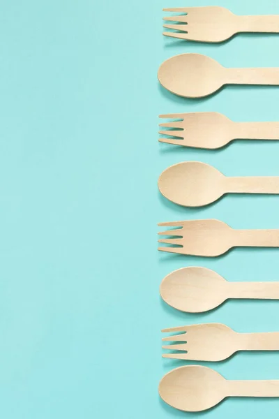 stock image Wooden disposable forks and spoons on a blue background, top view. Eco friendly disposable kitchen utensils, copy space. Flat lay. Spoons and forks laid out in a row on one side of the composition