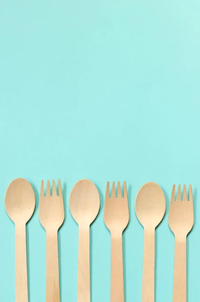 stock image Wooden disposable forks and spoons on a blue background, top view. Eco friendly disposable kitchen utensils, copy space. Flat lay. Spoons and forks laid out in a row on one side of the composition