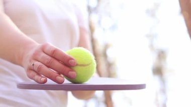 Açık hava oyunu. Tenis topuna aşağıdan yukarıya ahşap bir raketle vurmak. Tenis topu yaklaş. Bir kadın tenis raketiyle sarı topa vuruyor. Kız dışarıda spor aktivitelerine katılıyor.