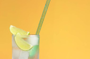 Parlak turuncu arka planda buzlu ve limonlu limonata. Soğuk içecekle yaz kokteyli. Uzayı kopyala Kamışla yakın plan iç.