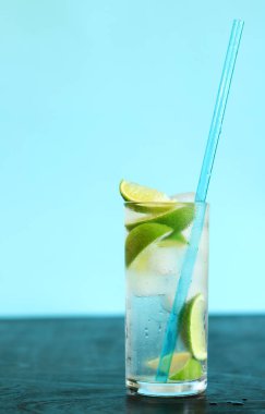 Açık mavi arka planda buzlu ve limonlu limonata. Karanlık bir masada soğuk bir içecekle yaz kokteyli. Kamışla taze içecek yakın çekim.