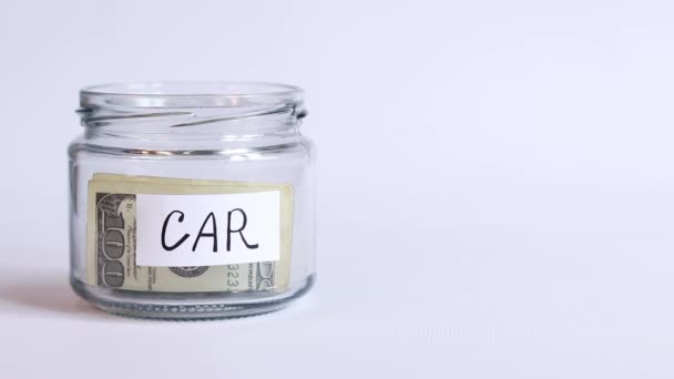 玻璃瓶与钱在白色背景特写 美元钞票掉进罐子里了 用美元买汽车的小猪银行 金融概念的积累 — 图库视频影像