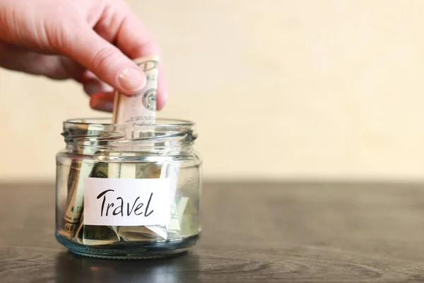 stock image Piggy bank with dollars for travel. Glass jar with money. The woman puts more money in the piggy bank. Selective focus