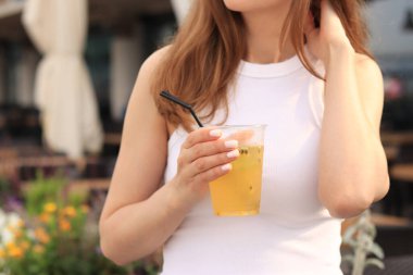 Tutkulu meyve limonatası. Yaz içeceği bir kızın ellerinde. Paket limonata. Soğuk limonata ve buzlu bir kadın eli bir yaz kafesine karşı.