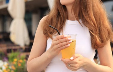 Tutkulu meyve limonatası. Yaz içeceği bir kızın ellerinde. Paket limonata. Soğuk limonata ve buzlu bir kadın eli bir yaz kafesine karşı.