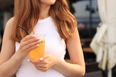 Tutkulu meyve limonatası. Yaz içeceği bir kızın ellerinde. Paket limonata. Soğuk limonata ve buzlu bir kadın eli bir yaz kafesine karşı.