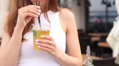 Tutkulu meyve limonatası. Yaz içeceği bir kızın ellerinde. Paket limonata. Soğuk limonata ve buzlu bir kadın eli bir yaz kafesine karşı.