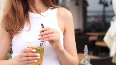 Tutkulu meyve limonatası. Yaz içeceği bir kızın ellerinde. Paket limonata. Soğuk limonata ve buzlu bir kadın eli bir yaz kafesine karşı.