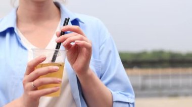 Tutkulu meyve limonatası. Yaz içeceği bir kızın ellerinde. Paket limonata. Nehir manzarasına karşı kadın eli buzlu soğuk limonata. Elinde içkiyle dans ediyor.