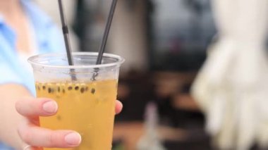 Kız limonata içmeyi teklif ediyor. Arka planda bulanık bir kızın elinde yaz içkisi. Bir kadın elinde soğuk limonata, bir sokak kafesine karşı. Yaz içecekleri reklamları. Tutku meyveli limonata.