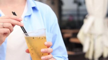 Tutkulu meyve limonatası. Yaz içeceği bir kızın ellerinde. Paket limonata. Soğuk limonata ve buzlu bir kadın eli bir yaz kafesine karşı.