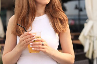 Tutkulu meyve limonatası. Yaz içeceği bir kızın ellerinde. Paket limonata. Soğuk limonata ve buzlu bir kadın eli bir yaz kafesine karşı.