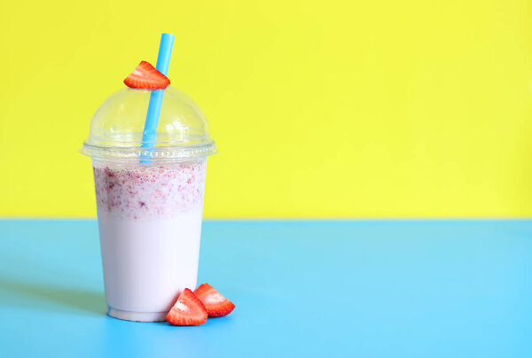 Strawberry smoothie with milk or yogurt. A plastic cup with a delicious strawberry smoothie on a bright yellow-blue background. Takeaway drink