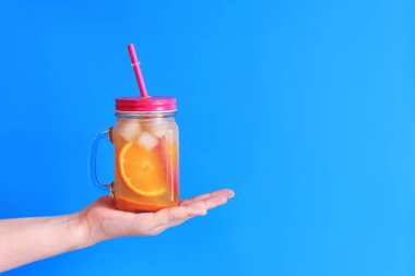 Paket limonata. Kızın avucundaki mason kavanozu. Mavi arka planda yaz içeceği. Portakal dilimleri ve buzlu ev yapımı limonata.