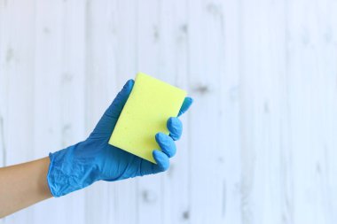 Hafif ahşap arka planda bulaşık yıkayan bir kadın eli için sünger. Lateks eldivendeki bir el ıslak temizleme için bir sünger tutar. Profesyonel temizlik. Boşluğu Kopyala