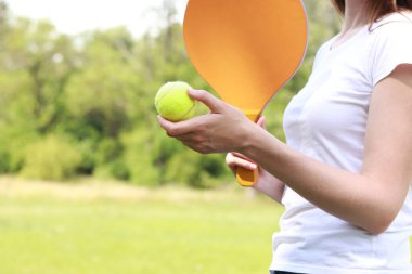 Doğanın arka planında tahta raketle paddleball oynamak. Tenis oynamak için tahta kürek ve bir kızın elinde top. Açık hava oyunları. Yakın plan.