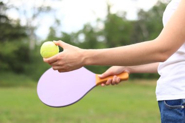 Doğanın arka planında tahta raketle paddleball oynamak. Tenis oynamak için tahta kürek ve bir kızın elinde top. Açık hava oyunları. Yakın plan.