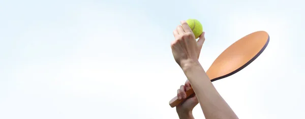 澄んだ空に対して木製のラケットでパドルボールを再生します ビーチテニス 白い背景の少女の手にテニスとボールを再生するための木製のパドル 屋外ゲーム — ストック写真