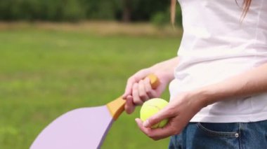 Doğanın arka planında tahta raketle paddleball oynamak. Tenis oynamak için tahta kürek ve bir kızın elinde top. Açık hava oyunları. Yakın plan.