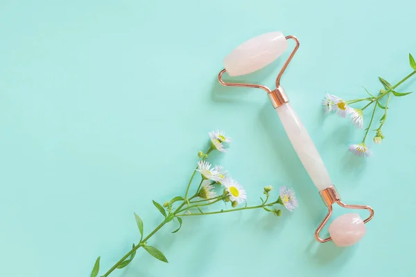 stock image Facial massage roller made of rose quartz on a blue background with chamomile flowers. Facial massager anti-wrinkle anti-aging skin care tool. Flat lay. Facial beauty massage, spa self care concept